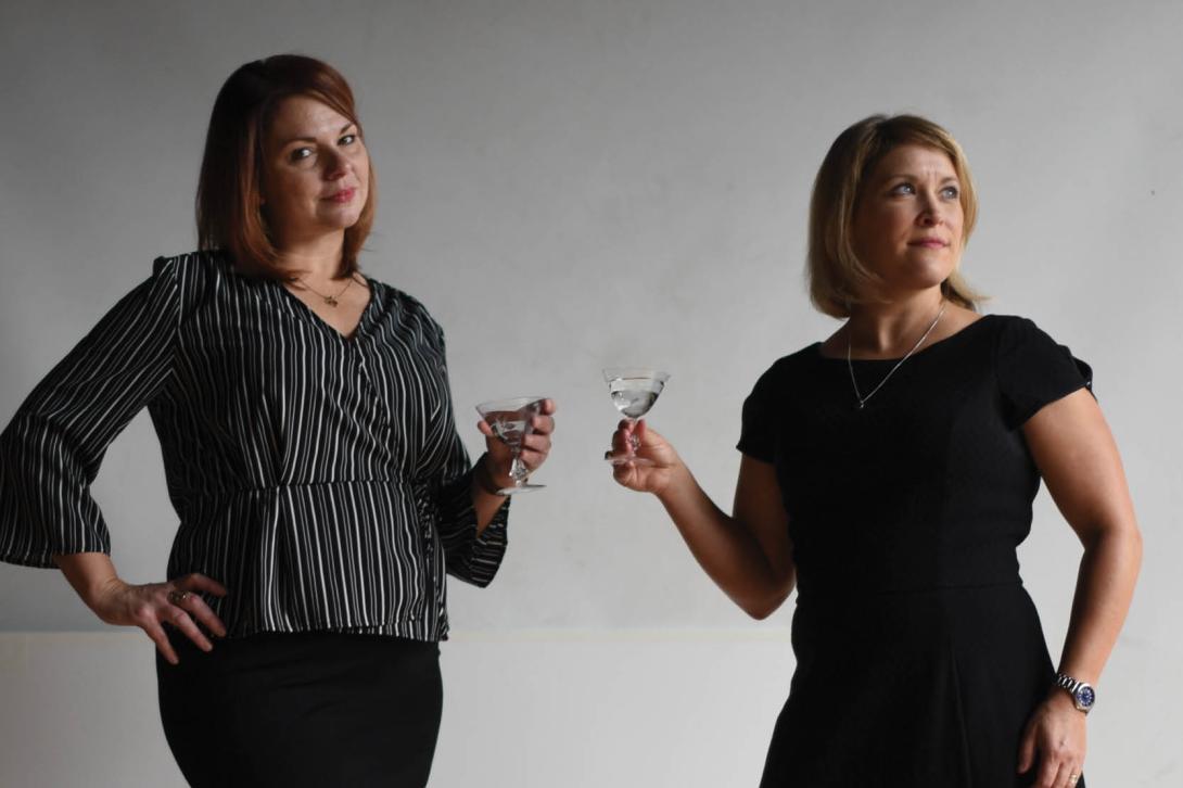 Jen and Karen, co-hosts of Speak Easy Podcast, toasting with cocktails in professional studio portrait.