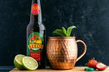 Lime and strawberry slices arranged around a bottle of ginger beer and a copper mug.