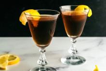 Two glasses of a dark brown cocktail, the Troubled Leisure, with lemon slices to garnish.