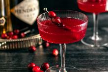 A ruby red liquid in a coupe glass, garnished with cranberries.