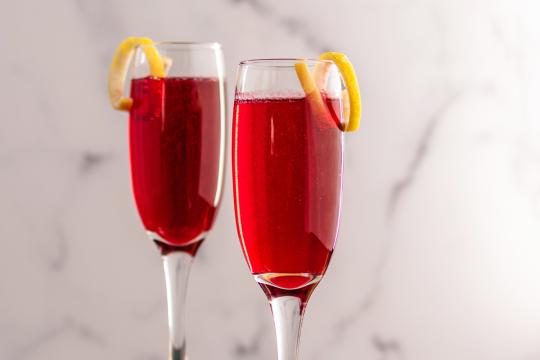 Two champagne flutes filled with a ruby red liquid toped with a lemon twist garnish