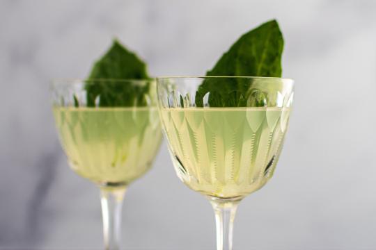 Pale yellow-green liquid in a cocktail glass, garnished with a basil leaf