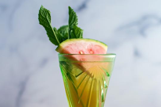 A green cocktail glass garnished with a slice of watermelon and a mint sprig