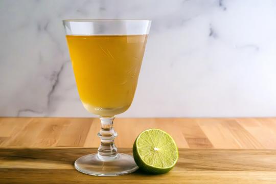 A goblet filled with amber liquid, with a half a lime resting against the bottom of the glass.