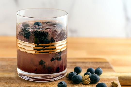 A short round glass filled with clear bubbly liquid, with muddled blueberries resting at the bottom.