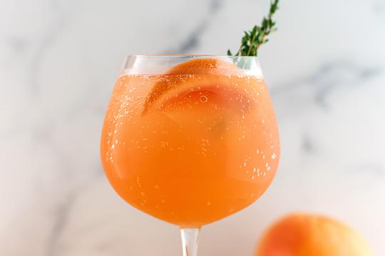Sparkling grapefruit cocktail with fresh grapefruit slice and thyme garnish in a stemmed glass. Refreshing summer drink on marble background
