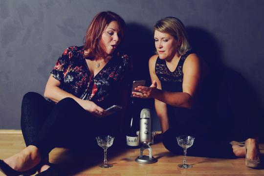 Jen and Karen sit on the floor against a gray wall. 