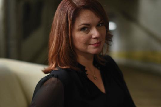 Jen, owner of Redhead Creative Consultancy and cohost of The Speak Easy Podcast, seated indoors in a black blouse for a professional branding portrait.