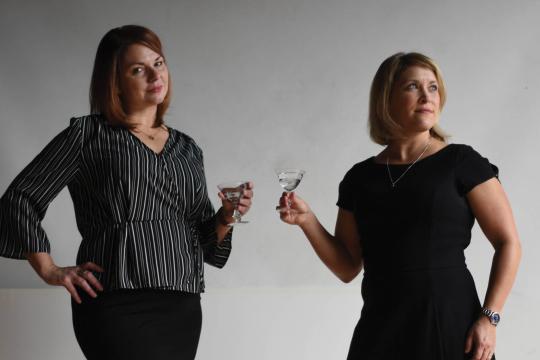 Jen and Karen, co-hosts of Speak Easy Podcast, toasting with cocktails in professional studio portrait.
