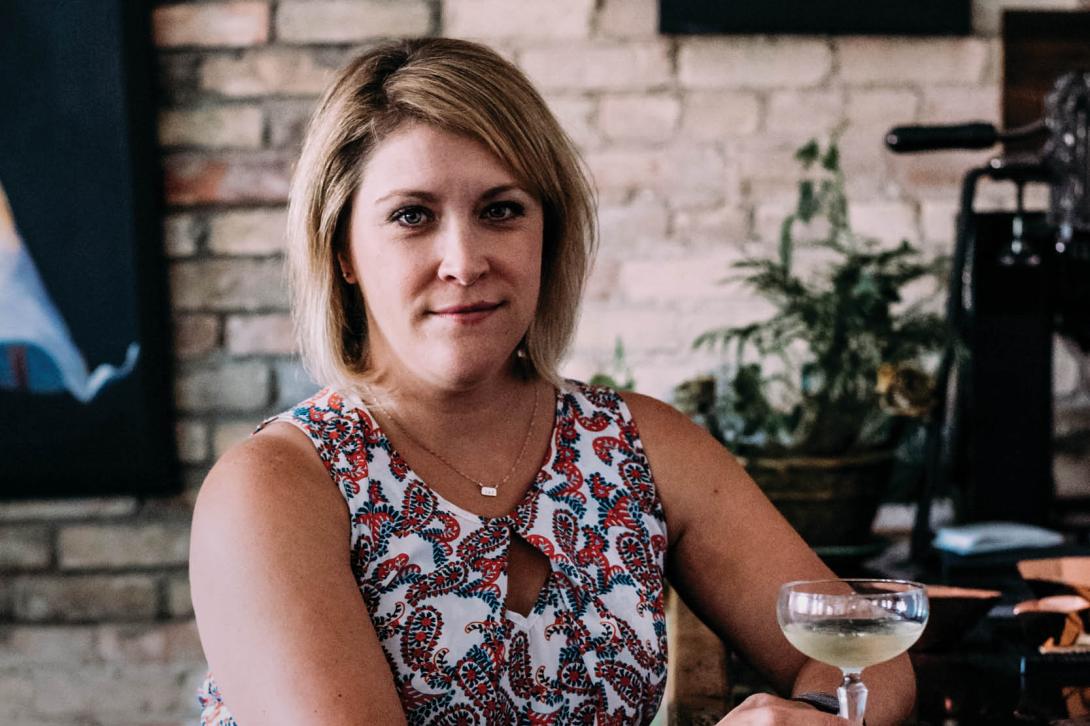 Co-host Karen Stefhl is sitting holding a cocktail glass, facing the camera