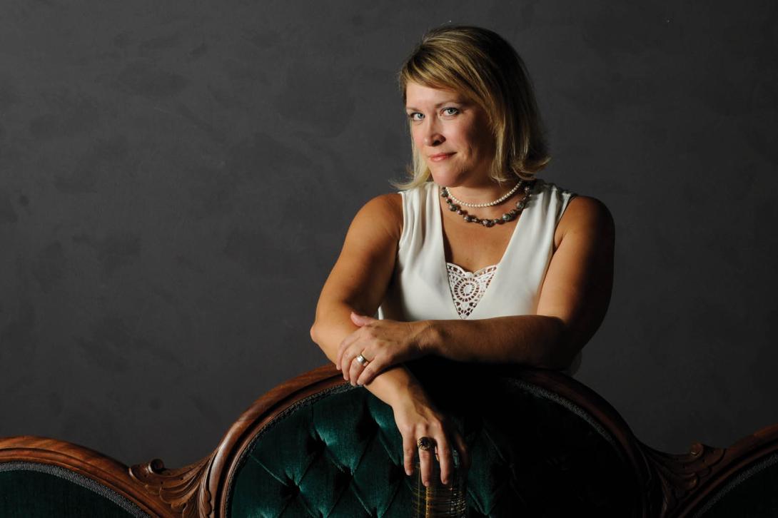 Karen, co-host of Speak Easy Podcast, professional portrait sitting on green velvet chair in studio setting